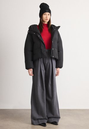 Giubbotto imbottito nero con cappuccio, top rosso aderente e pantaloni larghi grigi, abbinati a un berretto nero e scarpe nere. Tessuti lisci e vestibilità rilassata.