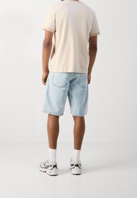 Beige bomuld t-shirt med korte ærmer, lyseblå denimshorts og grå sneakers med hvide detaljer. Simpelt design med afslappet pasform.