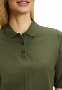 Olijfgroene polo shirt van gestructureerde stof, met een kraag en een knoopsluiting met drie knopen. Korte mouwen en een getailleerd ontwerp.