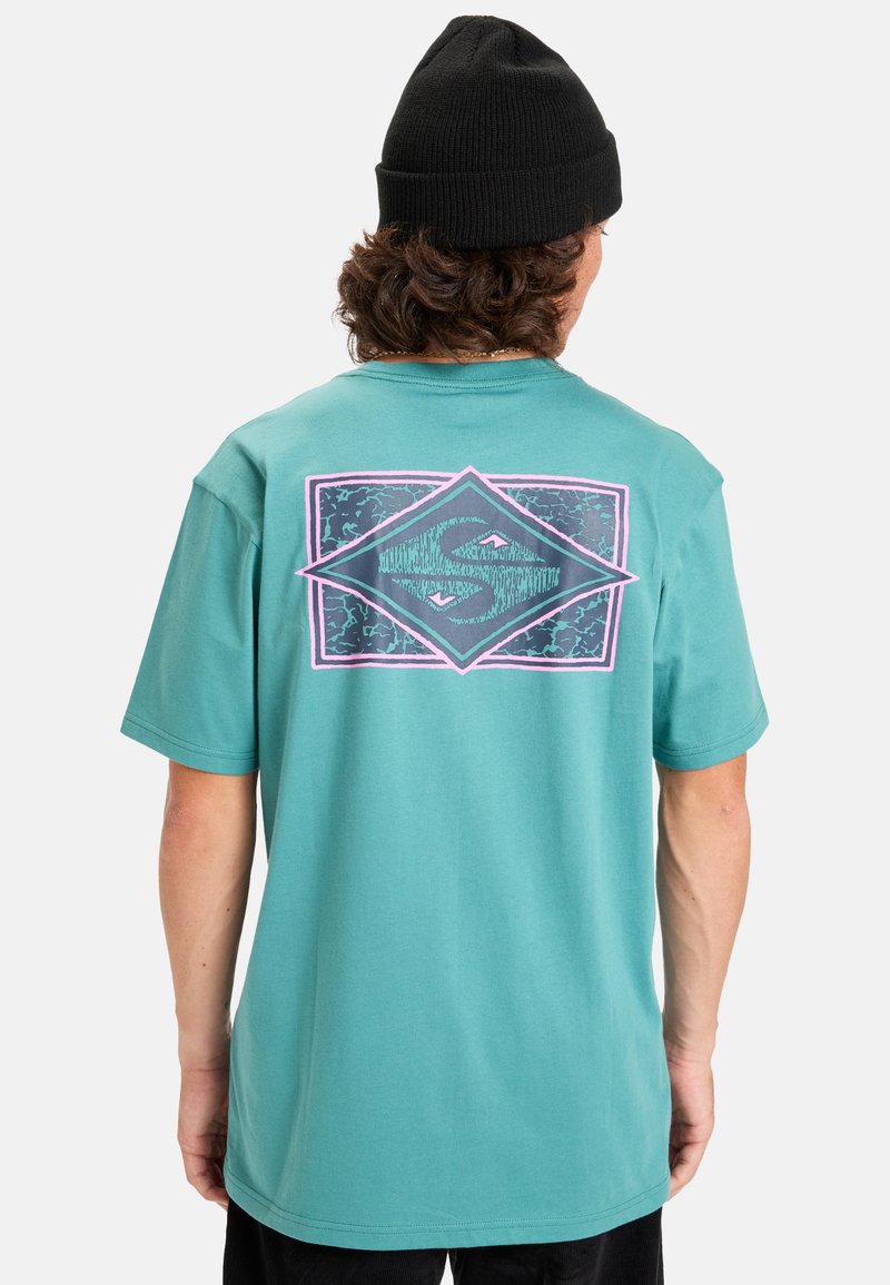 Tyrkysové bavlněné tričko s velkým grafikou na zadní straně v purpurové a černé barvě, se šikmým tvarem a vzorem vln.
