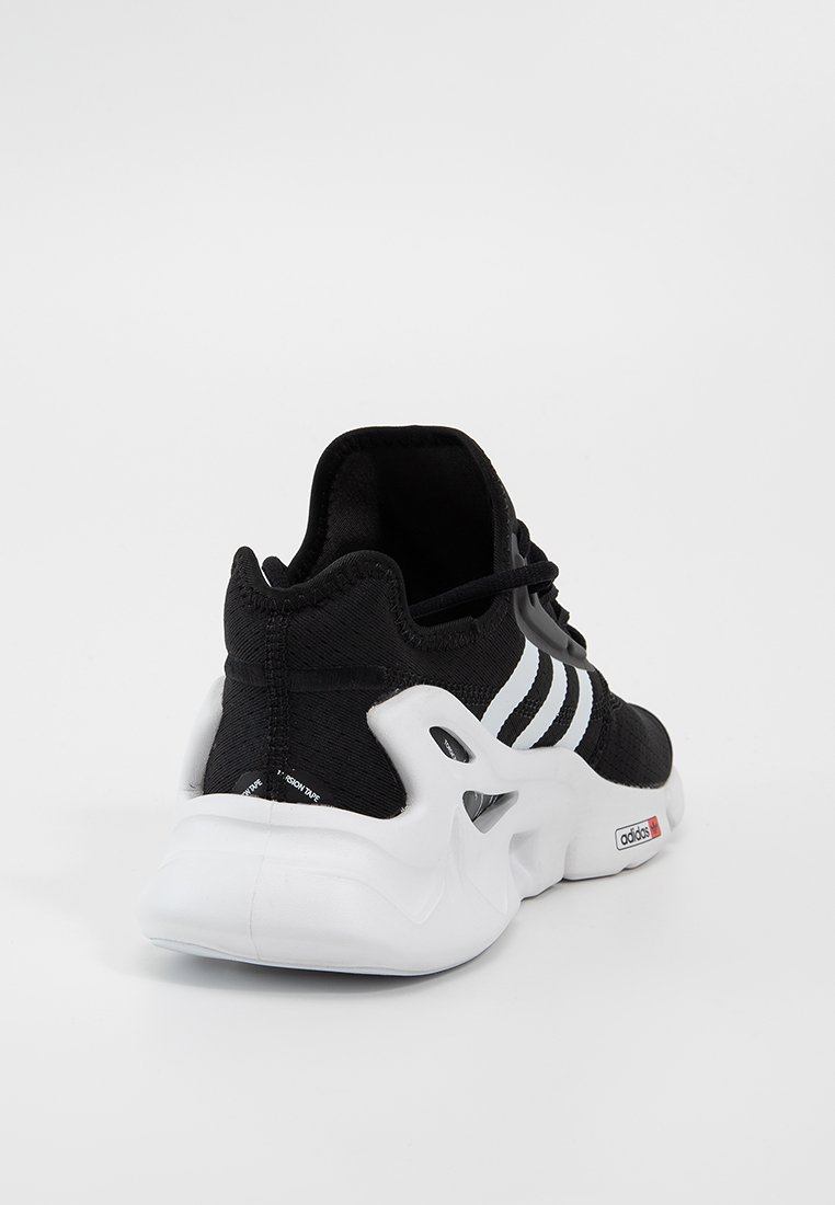 Svart mesh-sneaker med vadderad krage, vit gummisula och tre vita ränder på sidan. Texturerad ovandel för andningsförmåga.