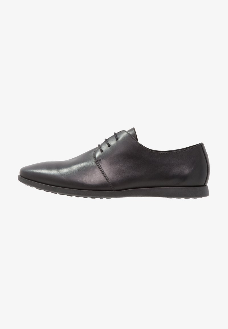 Chaussure habillée pour homme en cuir noir avec trois œillets, bout pointu et semelle en caoutchouc basse, montrée de profil vers la gauche.