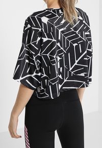 Svart och vit kortärmad crop-top med geometrisk mönstring och ett texturerat, ventilerande tyg, matchad med svarta leggings.