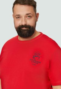 Rode katoenen t-shirt met een ronde halslijn en korte mouwen, met een donkerblauw grafisch ontwerp van een vis en tekst aan de voorkant.
