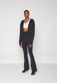 Zwarte rits hoodie, witte sportieve crop top, hoge zwarte leggings en zwarte sportschoenen. Gladde stof zonder zichtbare patronen.