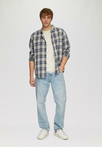 Kariertes Flanellhemd in Blau und Weiß über einem hellen T-Shirt, kombiniert mit hellblauen Jeans und weißen Sneakers. Lässig, lockere Passform.