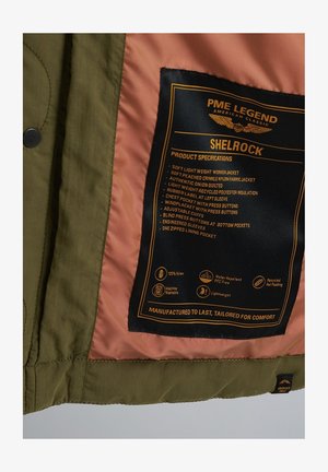 Chaqueta de trabajo de nylon verde oliva con un forro melocotón; incluye etiqueta de especificaciones del producto en negro y naranja, múltiples bolsillos y puños ajustables.