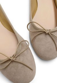 Ballerine beige in suede con punta rotonda, con un delicato dettaglio a fiocco e una finitura testurizzata lungo l'apertura.