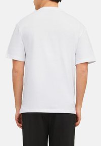Weißes T-Shirt mit kurzen Ärmeln aus Baumwolle, mit Rundhalsausschnitt. Die Rückseite ist schlicht und hat keine Muster oder Grafiken, und der Stoff hat eine glatte Textur.