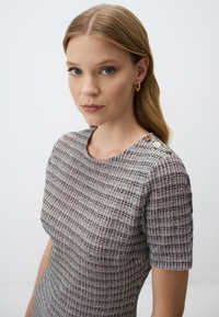 Robe grise à motif avec des manches courtes, présentant un tissu texturé et des accents de boutons dorés sur l'épaule. Design simple et ajusté.
