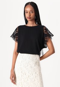 Top negro de manga corta con intrincados detalles de encaje. Tela suave, corte holgado, combinado con una falda de encaje marfil.