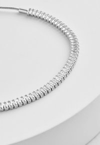 Collier en argent avec un design flexible, orné de plusieurs pierres précieuses transparentes disposées de manière symétrique. Texture lisse et finition réfléchissante.