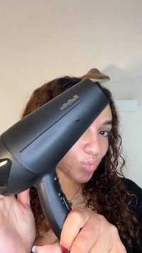 Sort håndholdt hårføner med et elegant design, utstyrt med et teksturert grep og kontrollknapper på siden. Synlig merkevarelogo.