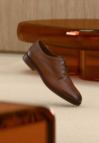 Καφέ δερμάτινο επίσημο παπούτσι με κομψό σχεδιασμό, μυτερή μύτη και έξι τρύπες για κορδόνια. Λείο υλικό, μινιμαλιστικές λεπτομέρειες και ανθεκτική σόλα.