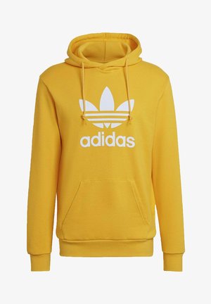 Sweat à capuche jaune Adidas avec logo trèfle blanc et texte sur le devant, poche kangourou avant et capuche à cordon réglable.