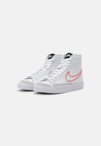Zapatillas altas de cuero blanco con acentos de gamuza gris, que cuentan con un swoosh rojo de Nike y cordones blancos, suela de goma texturizada.