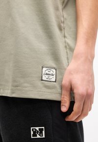 Gros plan sur une personne portant un t-shirt Nike vert clair et un pantalon Nike noir, montrant les logos Nike cousus sur les deux vêtements près des ourlets.