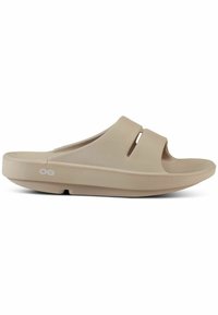 Beige slide sandals with a smooth, matte texture, wide upper straps featuring cut-out accents, and a ribbed footbed for grip.