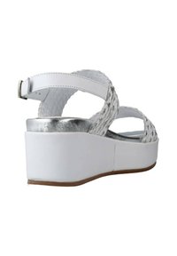 Sandaletta bianca con zeppa e tomaia intrecciata, dettagli in argento e cinturino alla caviglia. La suola è bianca con una finitura testurizzata. Progettata per comfort e stile.