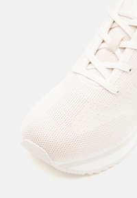 White athletic shoe featuring a textured knit upper, lightweight sole, and flat laces. Curved toe and minimalistic design with subtle accents.
