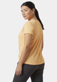 Tričko s krátkým rukávem v světleoranžové barvě z bavlny, s kulatým výstřihem a přiléhavým střihem. Zadní pohled ukazuje hladkou texturu a minimální detaily.