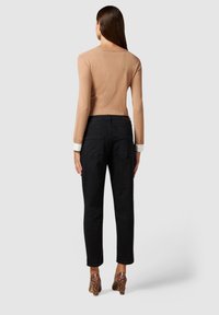 Top ajustado de manga larga en color beige con escote redondo, combinado con jeans negros ajustados. El conjunto se complementa con tacones de bloque con estampado de serpiente.