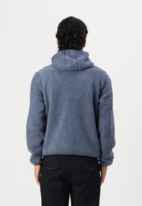 Fleece hoodie in soft, textured, light blue fabric with a hood, dropped shoulders, and a relaxed fit. Pairing with dark pants.