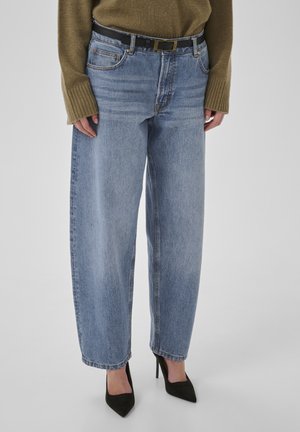 Jeans in denim blu chiaro con vestibilità ampia, vita alta, tasche frontali e cuciture visibili. Abbinati a scarpe nere con tacco alto.