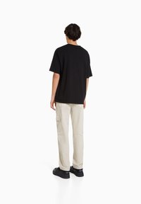 Black short-sleeve t-shirt, relaxed fit, with beige cargo pants featuring side pockets, and black sneakers. Minimalist design and no visible patterns.