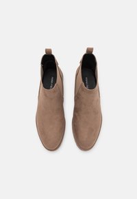 Par de botas de tobillo de ante marrón sin cordones con puntera redonda y tiradores, vistas desde arriba sobre un fondo blanco.