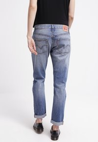 Keskitumma sininen farkut, joissa on suora lahje, käännettävät lahkeet ja takataskut, joissa on ommeltu V-muotoilu. Nahkainen brändilogo vyötäröllä.