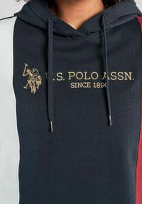 Granatowy hoodie z białą i czerwoną panelą, ozdobiony złotym haftowanym logo U.S. Polo Assn. oraz sznurkami z metalowymi końcówkami. Miękka tekstura materiału.