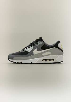 Страничен изглед на сива и бяла маратонка Nike Air Max с черни връзки и видима подметка с въздушна възглавница.
