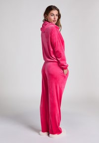 Roze velours trainingspak met een capuchon, met een comfortabele pasvorm en elastische manchetten. De broek heeft zijzakken en is gecombineerd met witte fluffy slippers.