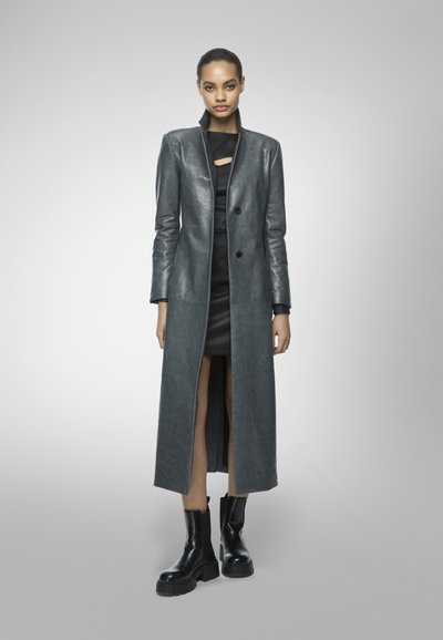 Long gray leather coat with a sleek design, featuring a high collar, two buttons, and a front slit, paired with a black dress and chunky boots.