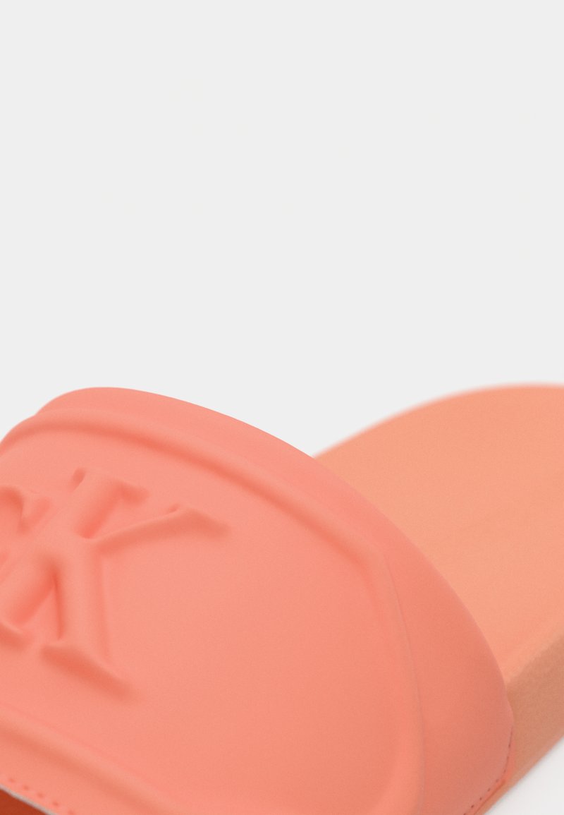 Chancla rosa hecha de goma suave, que cuenta con una correa texturizada con un logo en relieve y una plantilla acolchada para mayor comodidad.