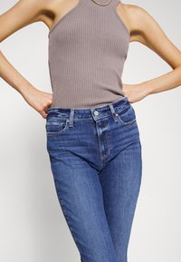 Harmaa resorillinen hihaton toppi yhdistettynä vartalonmyötäisiin sinisiin farkkuihin. Farkuissa on nappikiinnitys ja etupuolella lievästi haalistuneita kohtia.