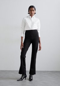 White button-up shirt with long sleeves, paired with high-waisted black flared pants and glossy black pointed-toe boots.