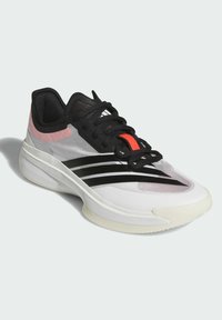 Scarpa sportiva bianca con dettagli neri e tomaia in mesh. Caratterizzata da tre strisce nere, dettagli rossi e un suola bianca testurizzata.