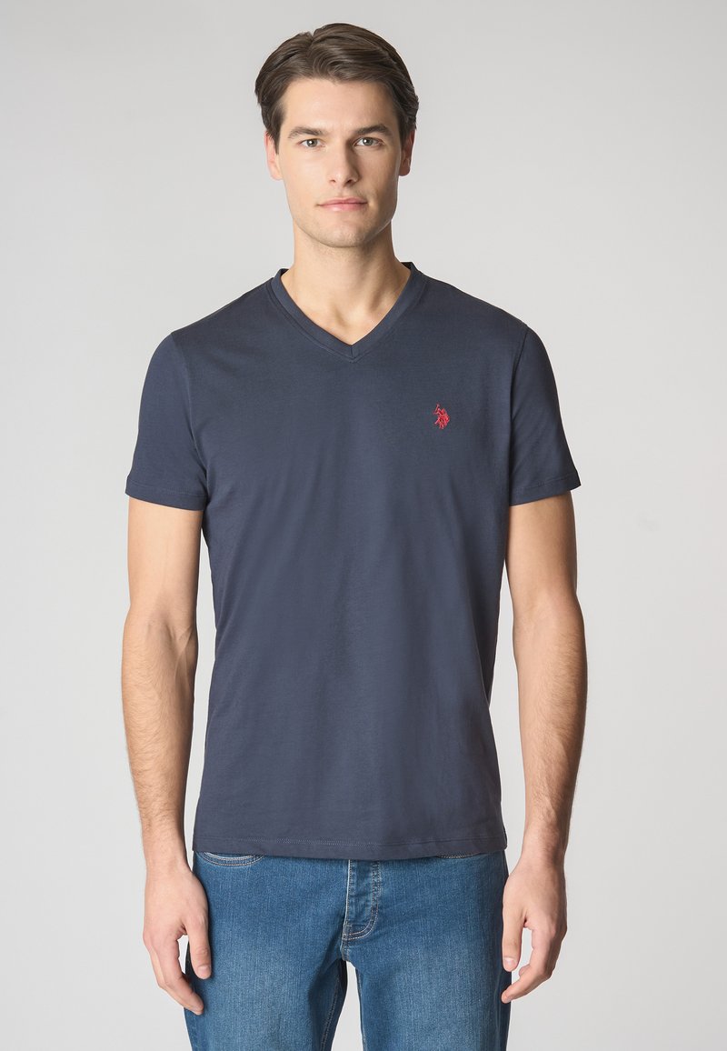 T-shirt a V blu realizzata in cotone, con maniche corte e un piccolo logo rosso sul lato sinistro del petto. Indossata con jeans blu.