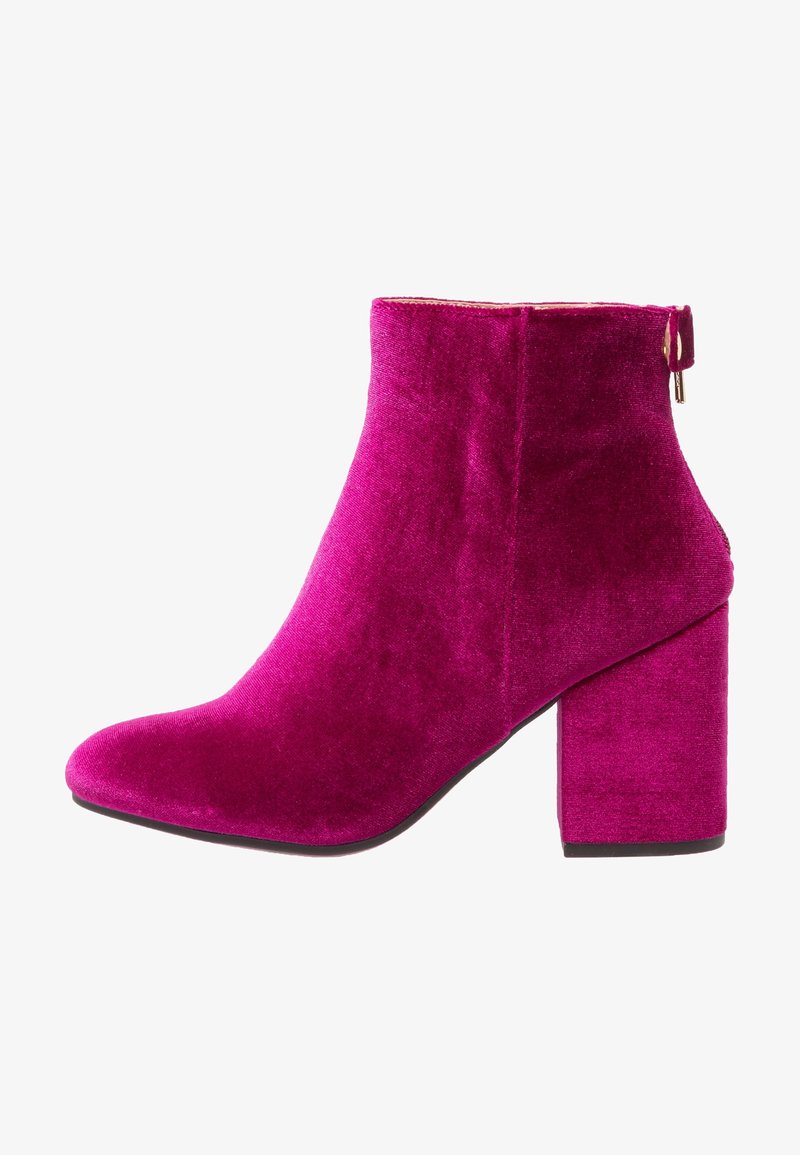 Botte en velours fuchsia montant à la cheville avec talon bloc et fermeture éclair latérale, montrant le profil gauche sur fond blanc.