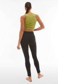 Leggings neri con vita alta e tasche posteriori, abbinati a un top a maniche corte verde a coste e cropped. Struttura liscia, design aderente.
