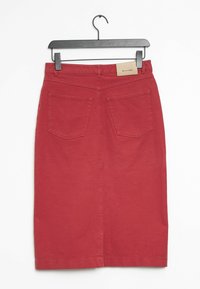 Gonna di jeans rossa con un design aderente, dotata di due tasche posteriori e un'etichetta in pelle in vita. Appesa a un gancio nero.