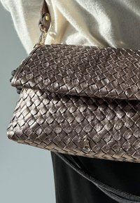 Sac à main en bronze métallisé tressé avec une fermeture à rabat et un petit accent logo. Comprend une bandoulière amovible et une texture lisse.