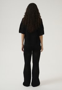 Outfit in maglia nera con una maglietta ampia e pantaloni svasati, caratterizzati da un motivo a trama aperta e un tessuto testurizzato.