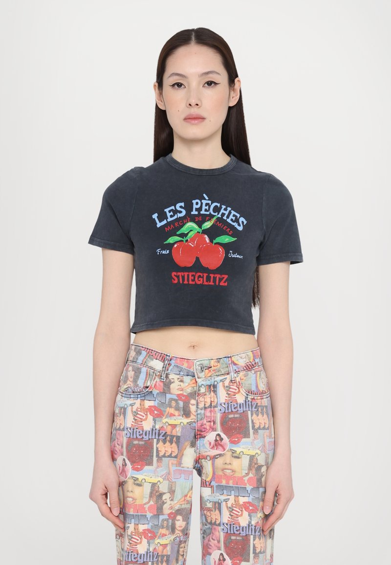 Black cropped t-shirt with contrast graphic text and cherry design. Pair of multicolored jeans featuring various images and patterns.