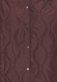 Burgundy quiltad jacka i tyg med vågmönster, sex metallknappar framtill, slät textur och subtil lyster.