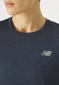Közeli kép egy sötétkék, textúrált New Balance pólót viselő személyről, akinek a jaw és nyak egy része látható.