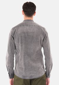 Camicia in denim grigia con yoke posteriore, maniche lunghe e polsini con bottone. Presenta una texture sbiadita e un orlo arrotondato.
