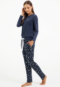 Granatowe piżamy z długim rękawem i okrągłym dekoltem oraz dopasowanymi spodniami w biały wzór gwiazdek i sznurkiem w pasie.